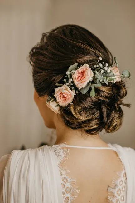 Elegant bridal hairstyle showcasing an updo adorned with pink roses and greenery.
